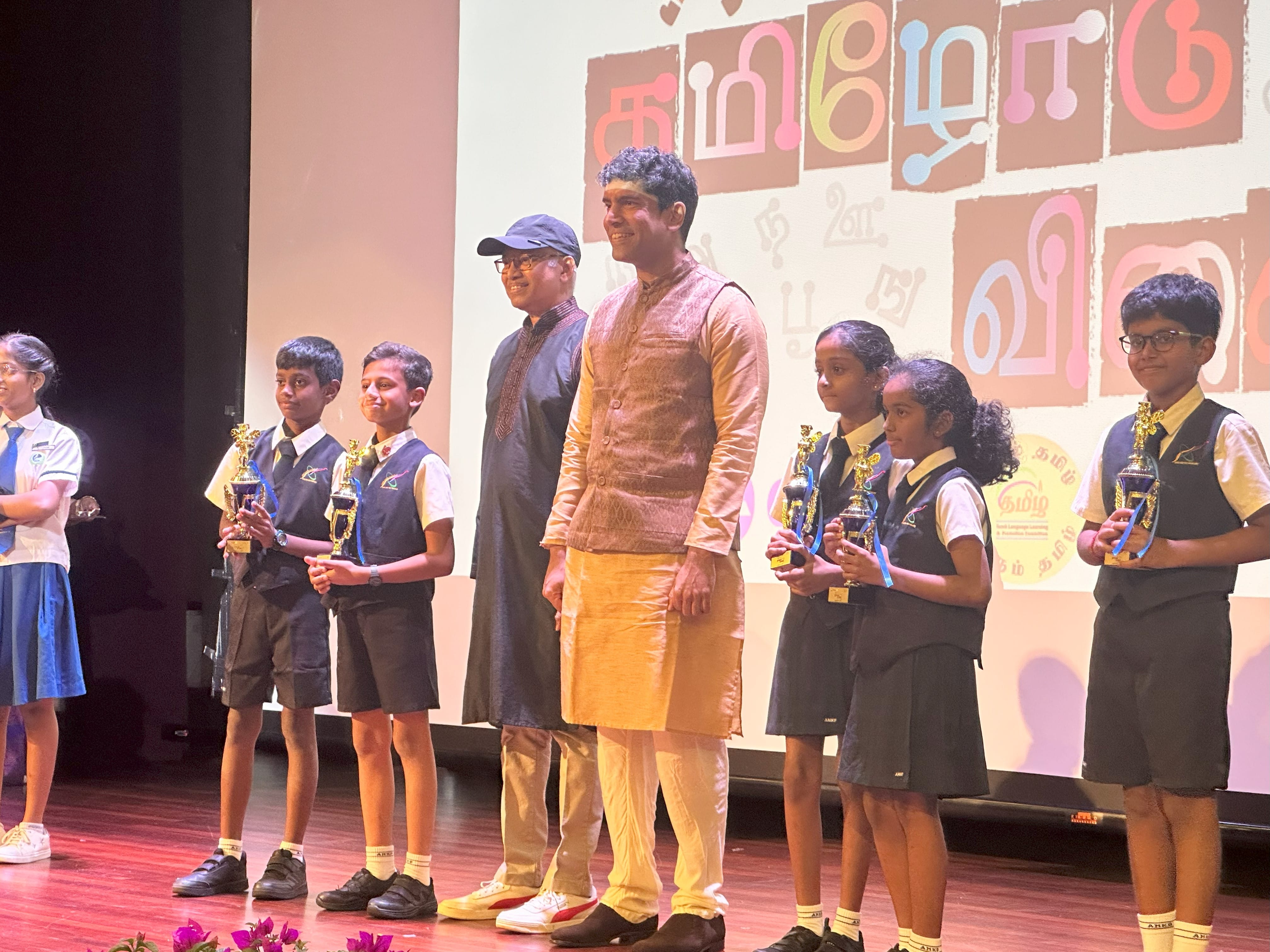 Photo of GOH and students holding on to their trophies on stage